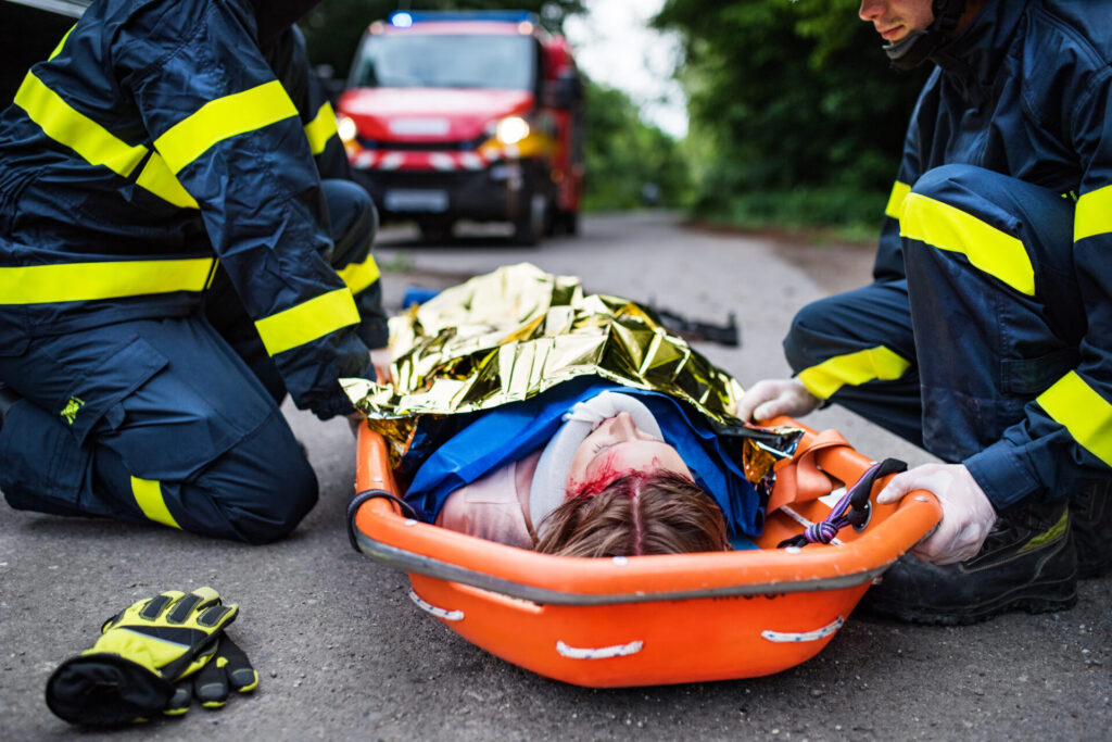 An injured woman in a plastic stretcher after a car accident, covered by thermal blanket.