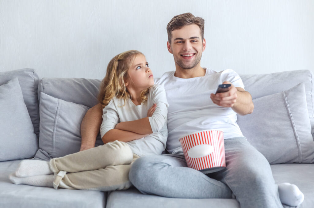 smiling father watching tv show while his daughter mad at him