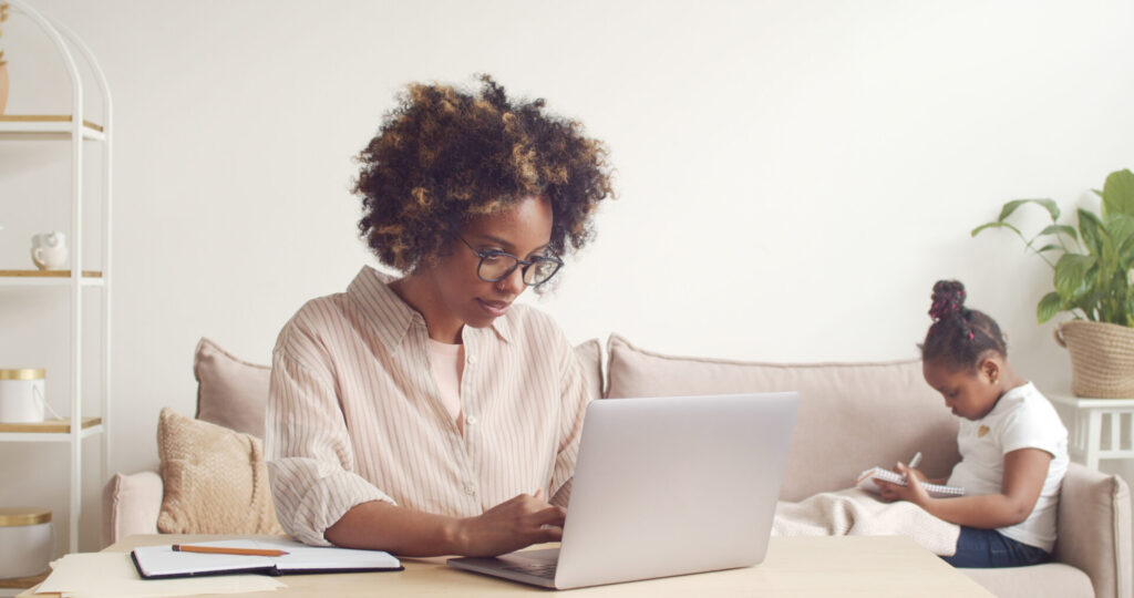 Pretty young african woman working on laptop online to support own child